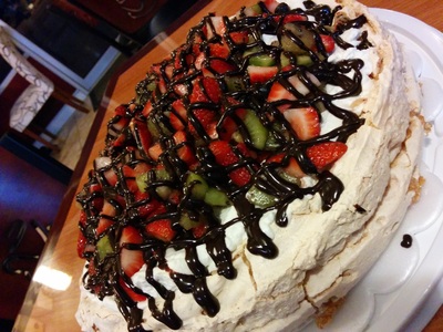 Pavlova with fresh kiwi, strawberries and blueberries, topped with ganache drizzle